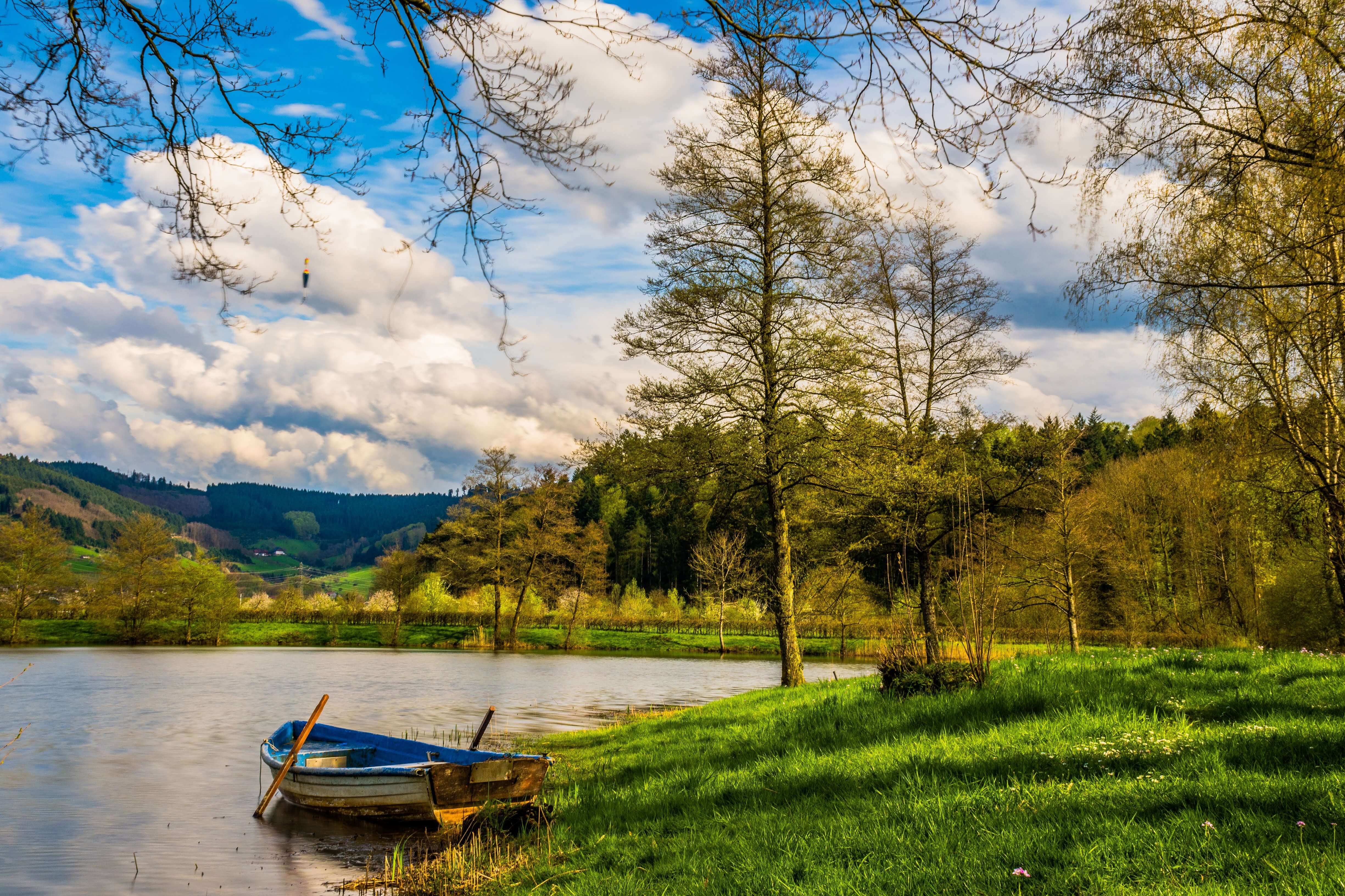 A wooden rowboat rests at the grassy edge of a calm lake surrounded by forested hills in Chile's Lake District. 