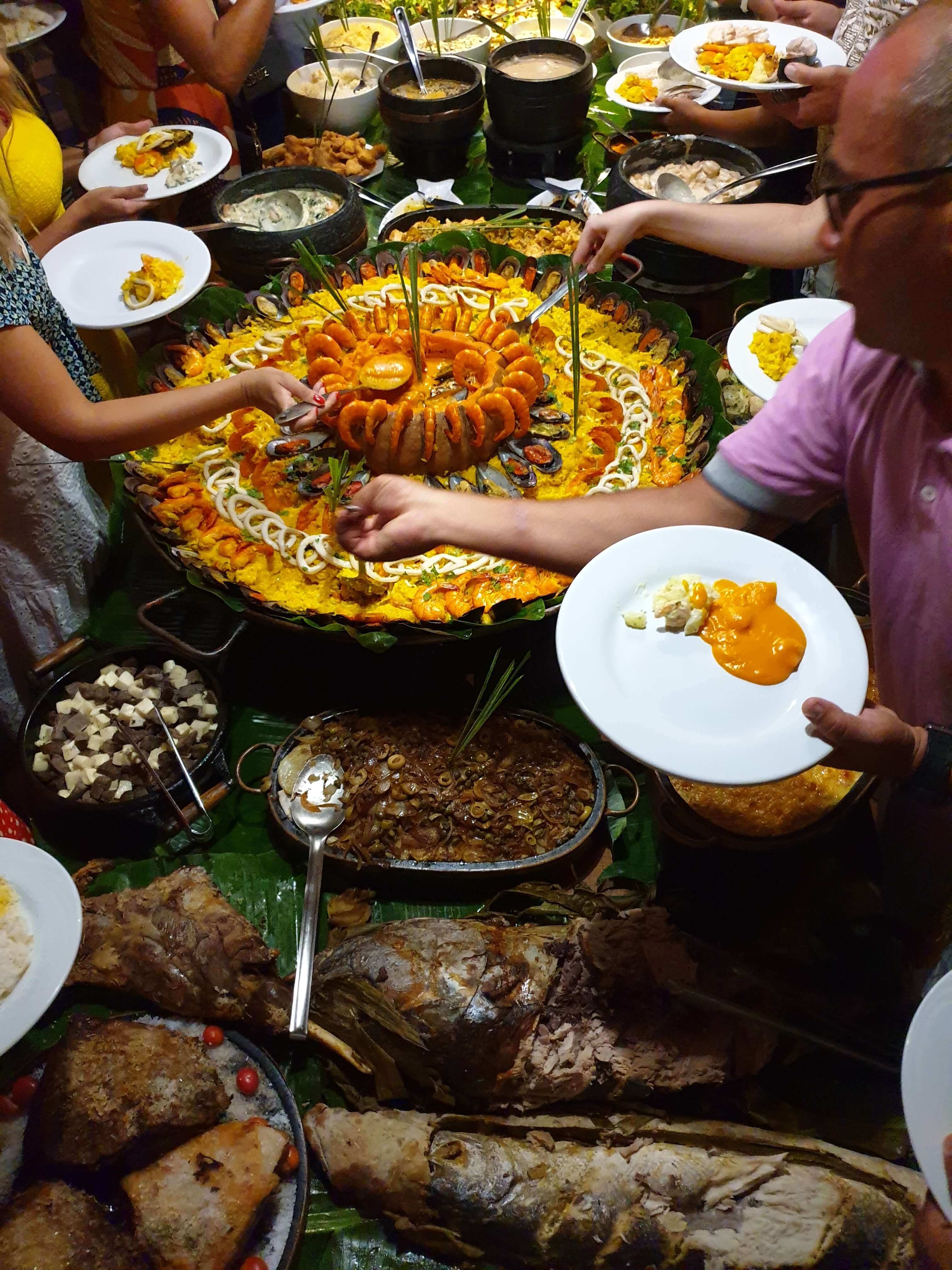 People serving themselves from a vibrant Brazilian seafood buffet with shrimp, rice and tropical dishes in Fernando de Noronha. 