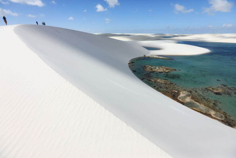 Sweeping view of Lencois Maranhenses with white sand dunes and vibrant lagoons under a bright blue sky. 