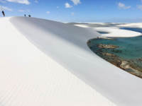 Sweeping view of Lencois Maranhenses with white sand dunes and vibrant lagoons under a bright blue sky. 