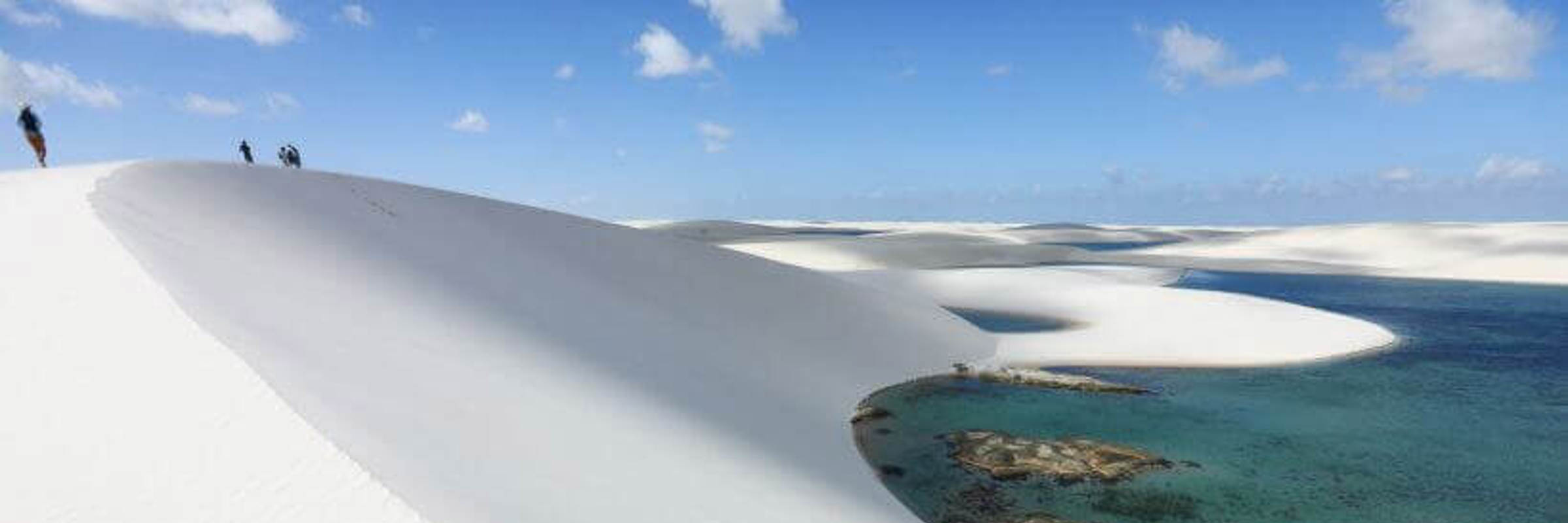 Sweeping view of Lencois Maranhenses with white sand dunes and vibrant lagoons under a bright blue sky. 
