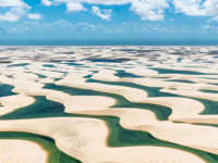 Aerial view of Lencois Maranhenses' white sand dunes and emerald lagoons beneath a vibrant summer sky. 