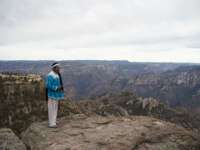Tarahumara man in traditional clothing stands on a cliff edge overlooking the dramatic Copper Canyon in northern Mexico. 