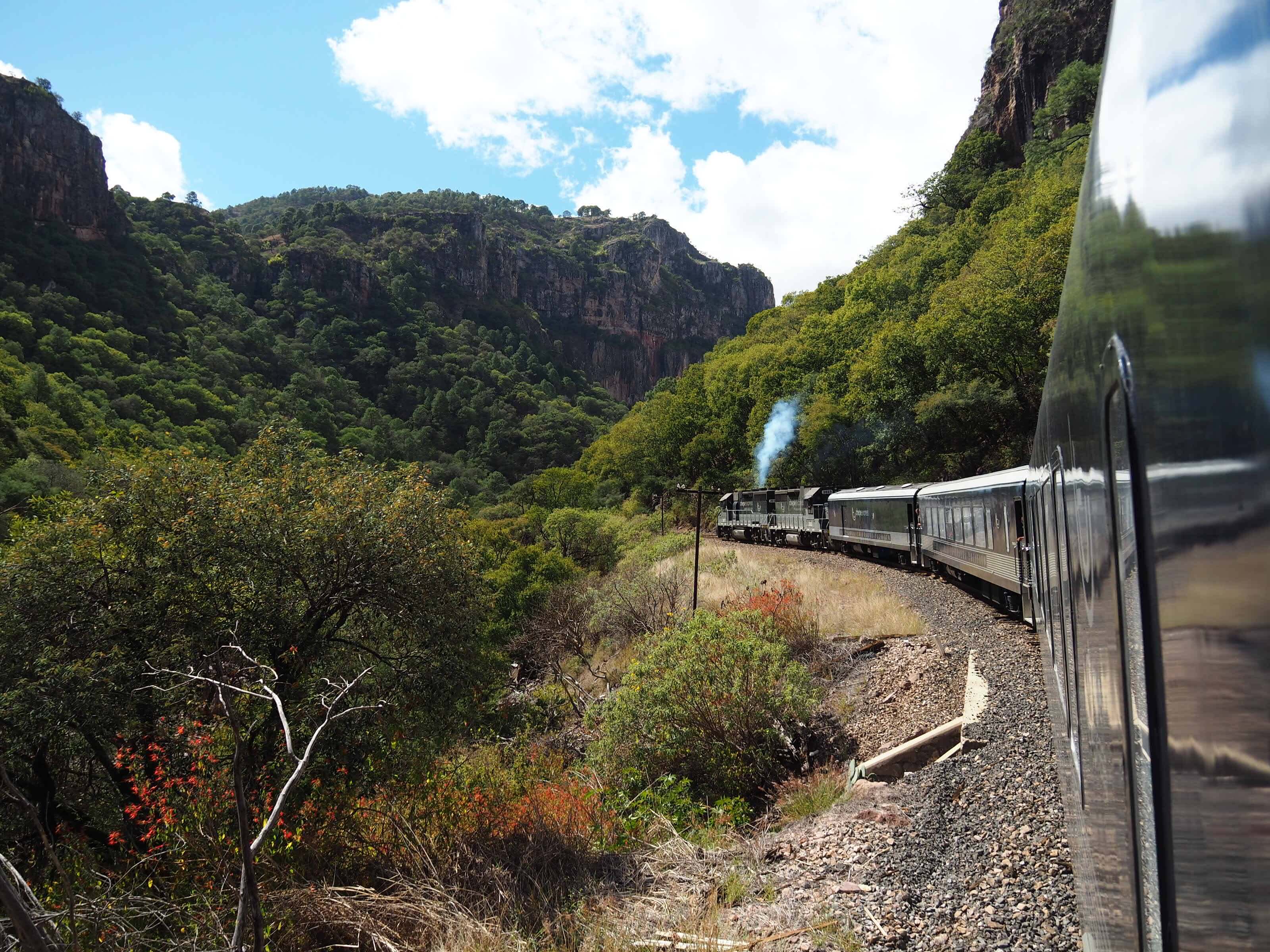 El Chepe train curving through the mountains and lush canyons of Mexico's Copper Canyon. 