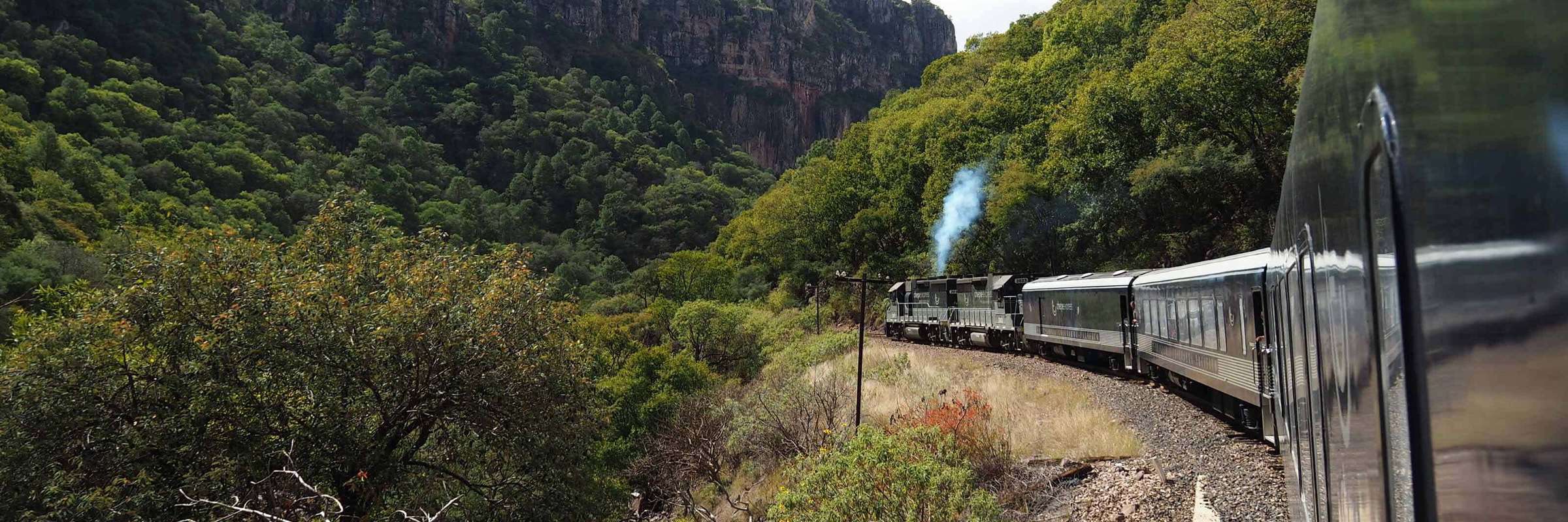 El Chepe train curving through the mountains and lush canyons of Mexico's Copper Canyon. 