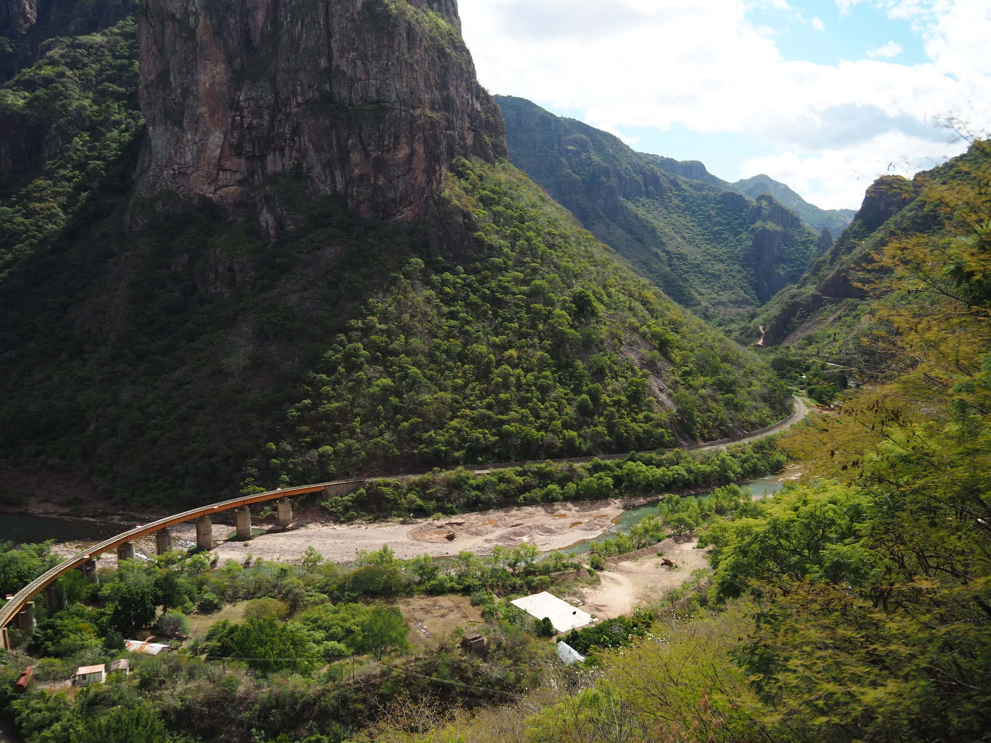 Railway bridge crossing a canyon river with dramatic cliffs and lush green mountains in Mexico's Copper Canyon. 