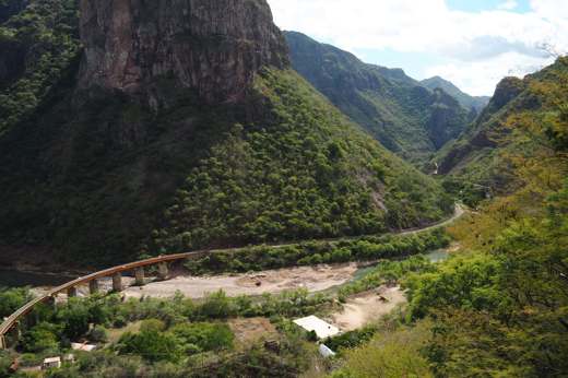 Railway bridge crossing a canyon river with dramatic cliffs and lush green mountains in Mexico's Copper Canyon. 