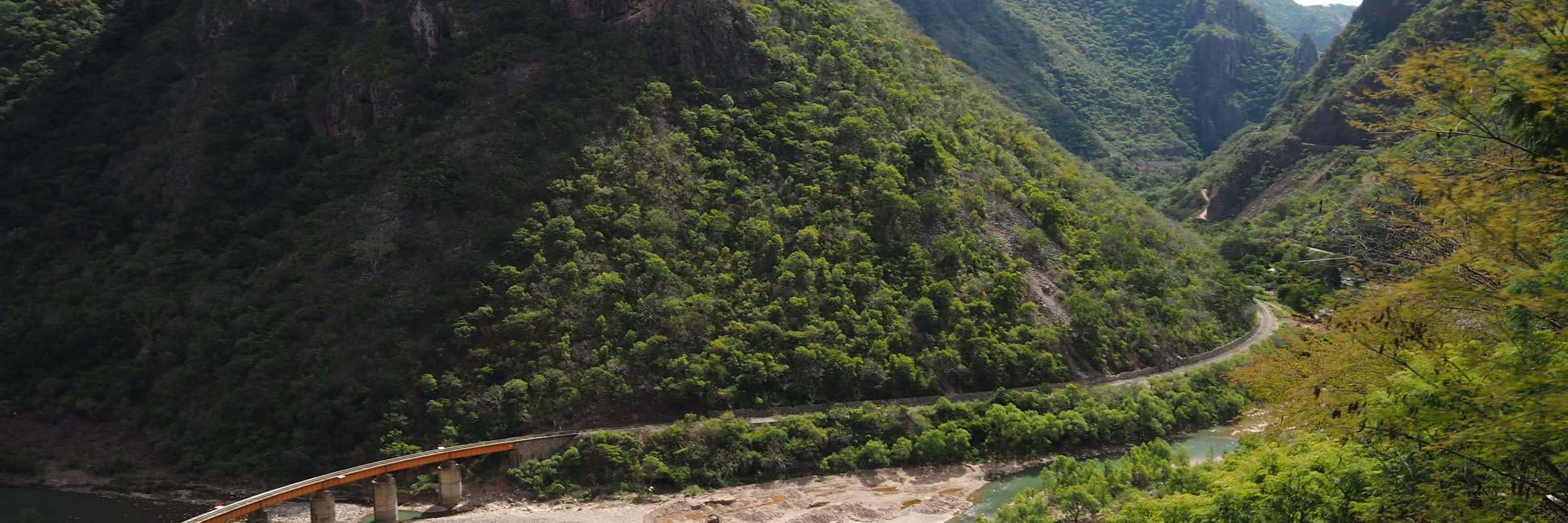 Railway bridge crossing a canyon river with dramatic cliffs and lush green mountains in Mexico's Copper Canyon. 