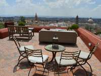 Terrace view over San Miguel de Allende, Mexico, with patio chairs and  a cityscape featuring church domes and skyline. 