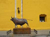 Bronze bull statue stands proudly against a vivid yellow wall in San Miguel de Allende, celebrating Mexican heritage. 
