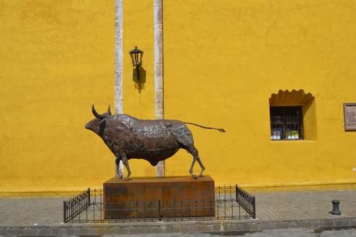 Bronze bull statue stands proudly against a vivid yellow wall in San Miguel de Allende, celebrating Mexican heritage. 