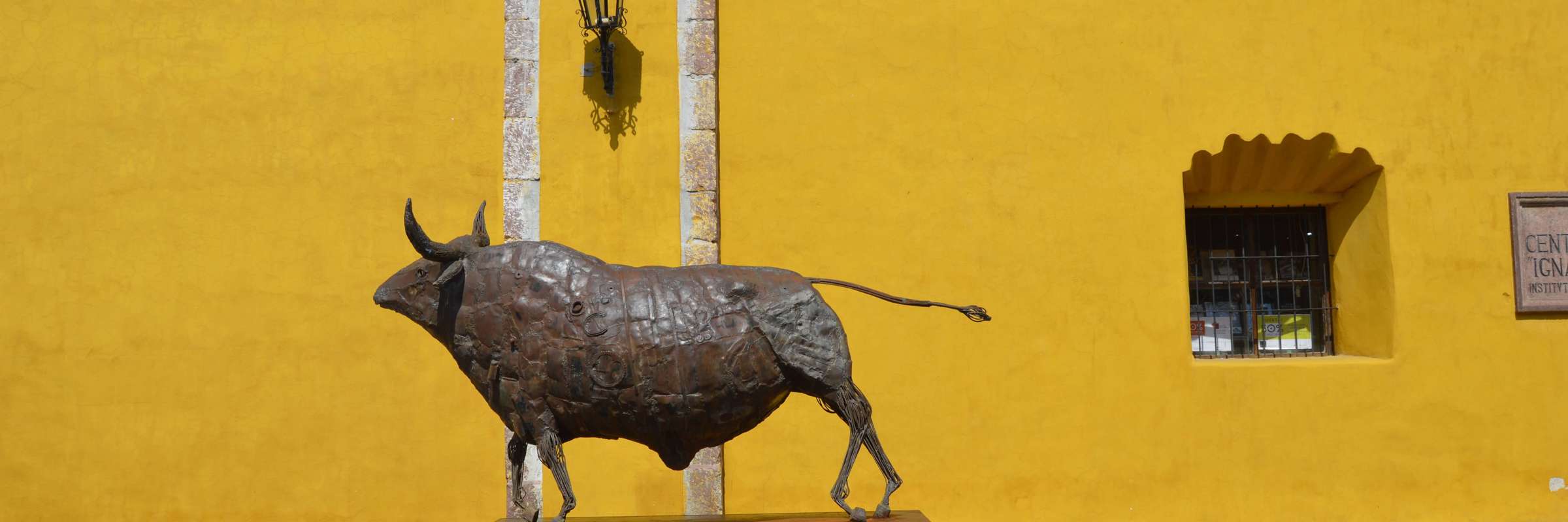 Bronze bull statue stands proudly against a vivid yellow wall in San Miguel de Allende, celebrating Mexican heritage. 