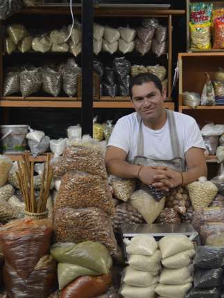 Friendly vendor in San Miguel de Allende sits among sacks of grains and spices, under the gaze of the Virgin of Guadalupe. 