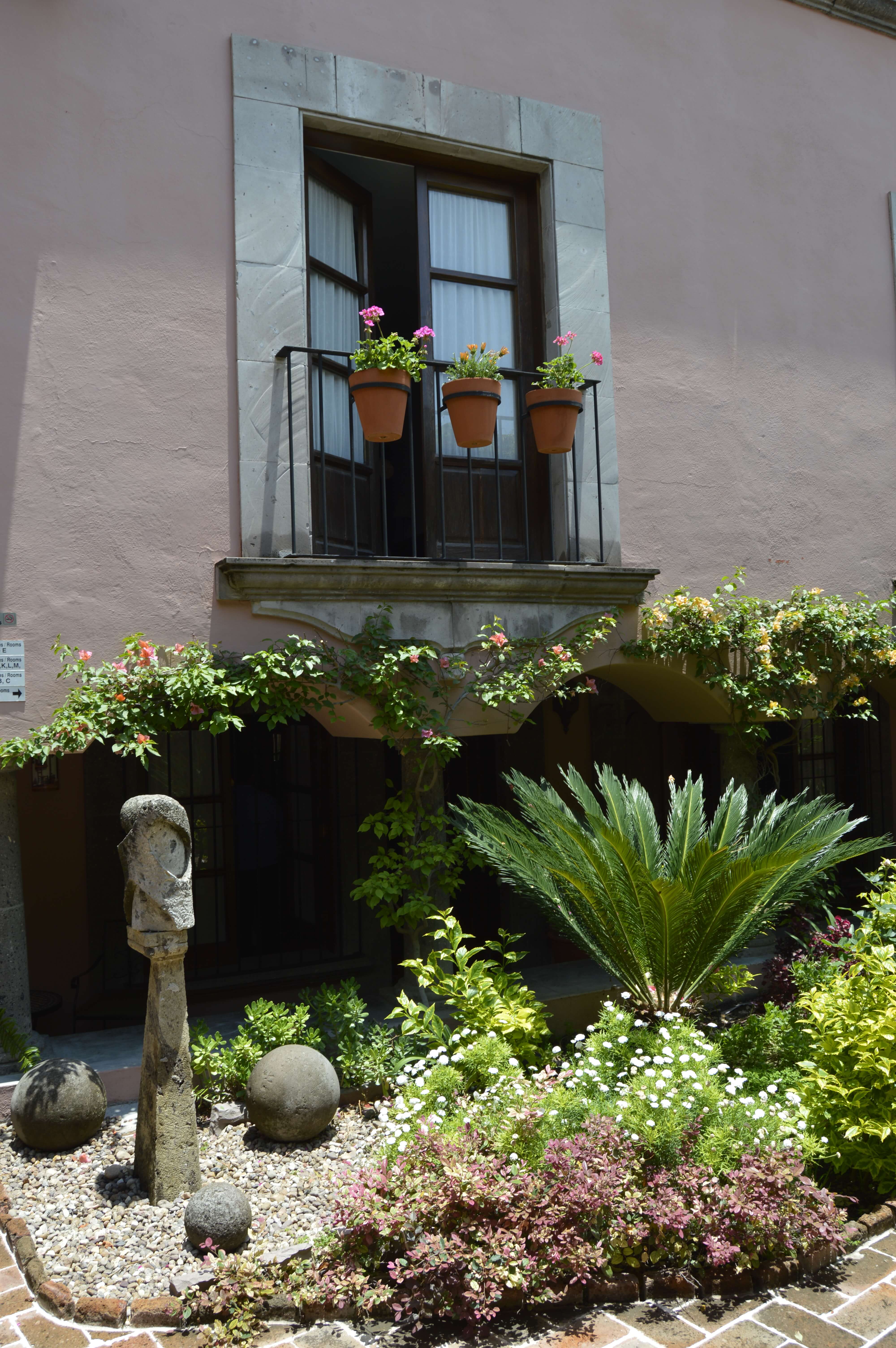 Charming courtyard with lush plants, stone sculpture, and flower-filled balcony in San Miguel de Allende, Mexico. 