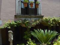 Charming courtyard with lush plants, stone sculpture, and flower-filled balcony in San Miguel de Allende, Mexico. 