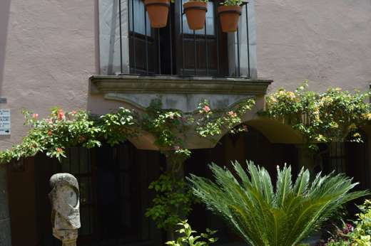 Charming courtyard with lush plants, stone sculpture, and flower-filled balcony in San Miguel de Allende, Mexico. 