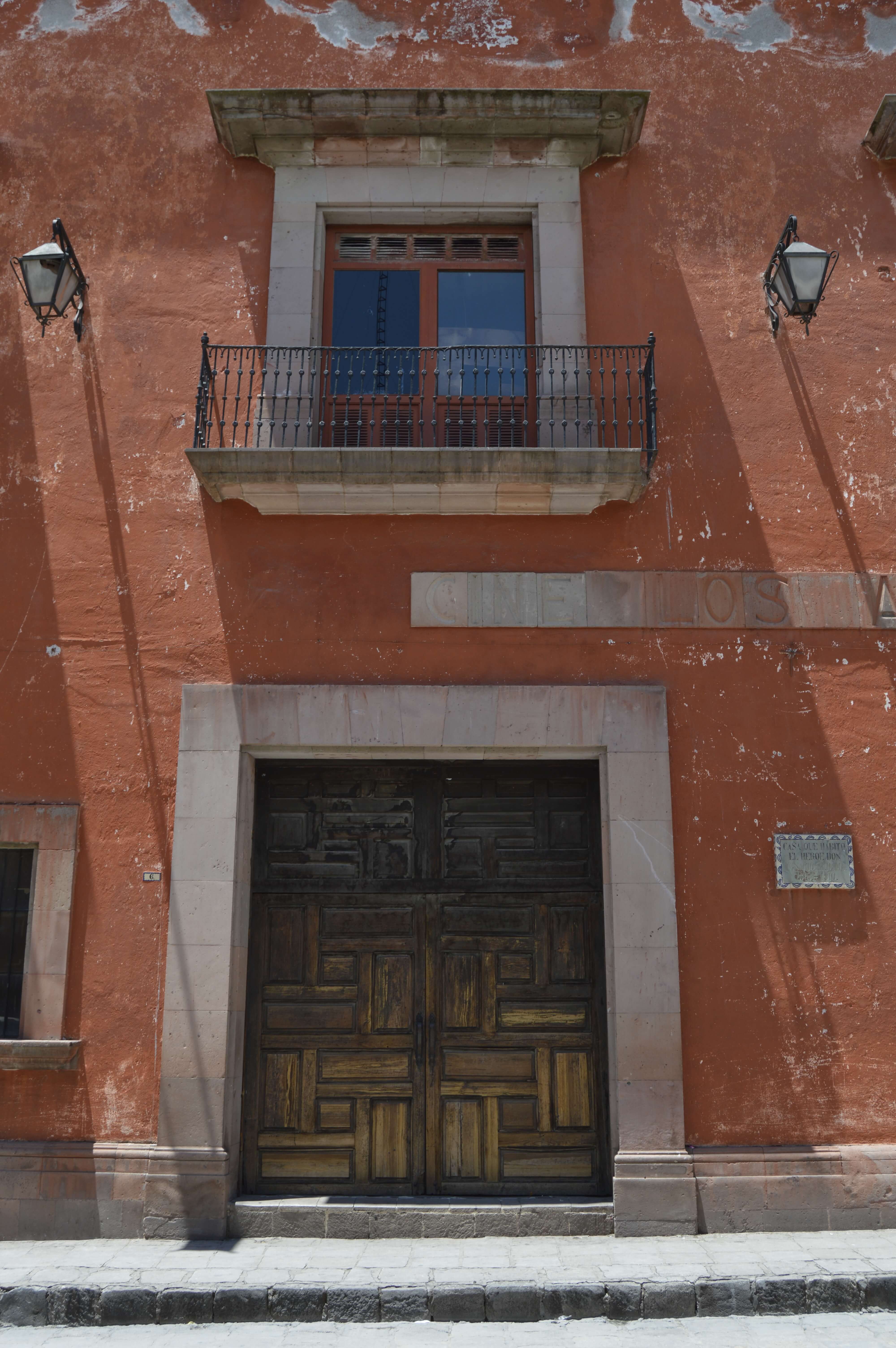 Weathered red colonial facade with wooden door, balcony, and wall lanterns in San Miguel de Allende, Mexico. 