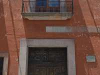 Weathered red colonial facade with wooden door, balcony, and wall lanterns in San Miguel de Allende, Mexico. 