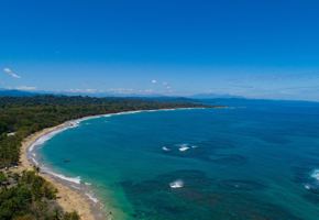 An aerial view of the sweeping Caribbean shoreline at Le Cameleon near Puerto Viejo, edged by lush rainforest. 