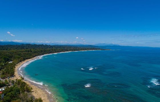 An aerial view of the sweeping Caribbean shoreline at Le Cameleon near Puerto Viejo, edged by lush rainforest. 