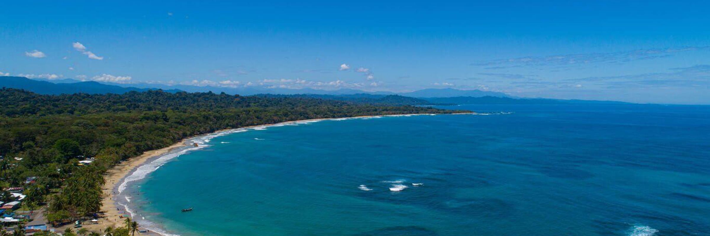 An aerial view of the sweeping Caribbean shoreline at Le Cameleon near Puerto Viejo, edged by lush rainforest. 