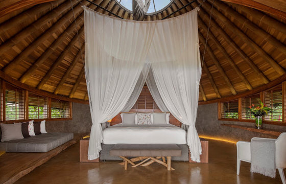 Spacious canopy bedroom with wooden interiors and panoramic jungle views at Origins Lodge. 