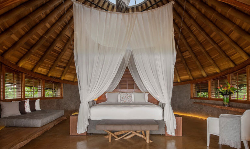 Spacious canopy bedroom with wooden interiors and panoramic jungle views at Origins Lodge. 