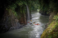 A group of Kayakers navigates the narrow canyon of the Pacuare River, surrounded by lush rainforest cliffs.