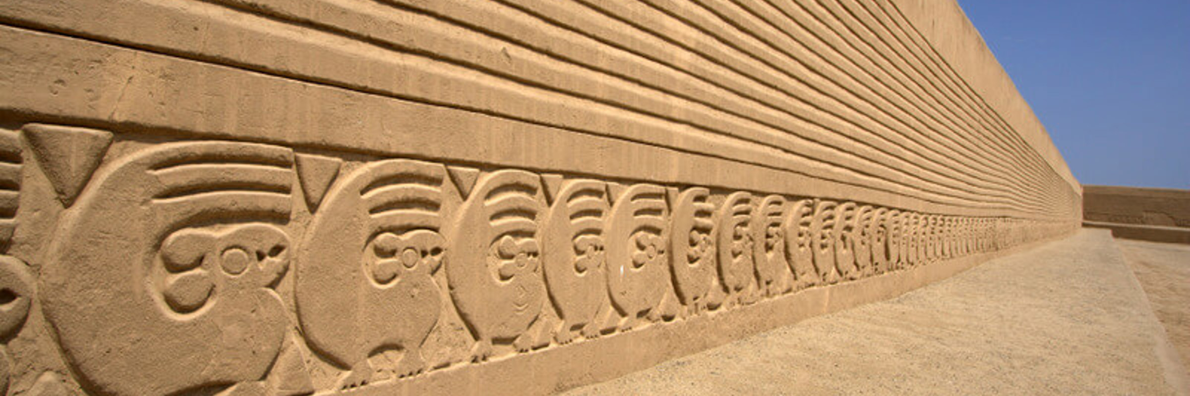 Intricate adobe carvings stretch along Chan Chan's ancient walls under Peru's desert sun. 