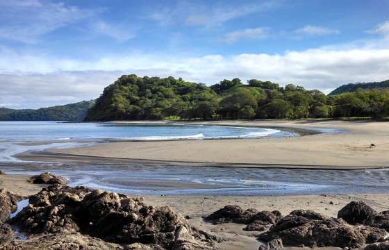 Quiet cove with rocky outcrops and golden sand on the Papagayo Peninsula under a clear blue sky. 
