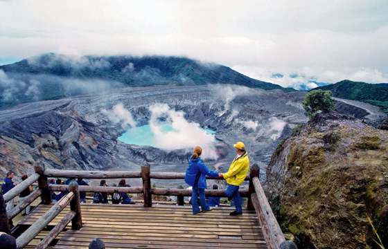 Visitors gaze into the steaming turquoise crater of Poas Volcano from a dramatic viewing deck. 