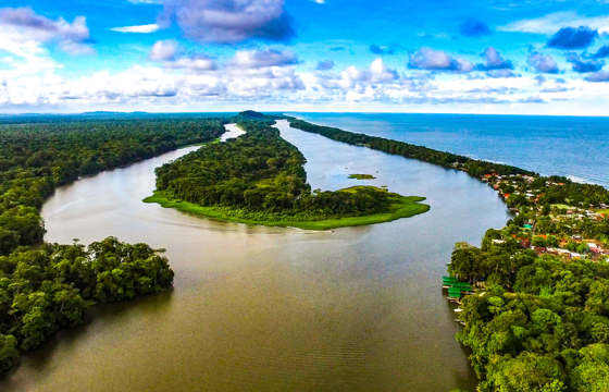 An aerial view captures the winding Tortuguero canals merging into the Caribbean Sea, framed by lush rainforest and coastal villages on Costa Rica's northeastern shore. 