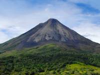 Majestic view of Arenal Volcano with lush greenery in the foreground and clear sky above. 