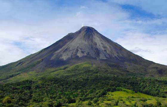 Majestic view of Arenal Volcano with lush greenery in the foreground and clear sky above. 