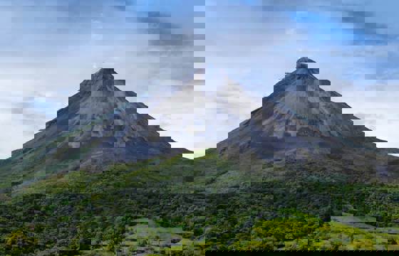 Majestic view of Arenal Volcano with lush greenery in the foreground and clear sky above. 