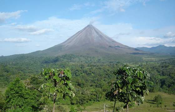 Arenal's symmetrical peak rises over rolling green hills under the clear skies of Costa Rica. 