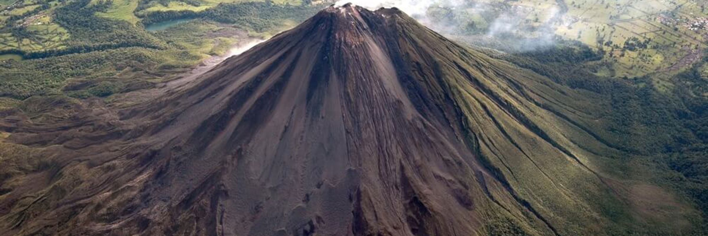 A dramatic aerial shot captures Arenal Volcano's perfect cone rising above rugged lava terrain. 