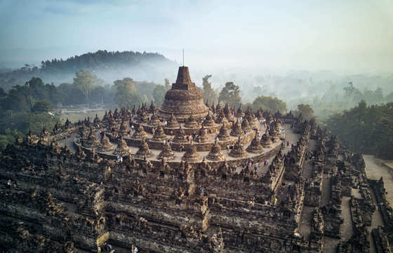 Borobudur Temple in Central Java, Indonesia bathed in soft morning light with misty forest in the background. 