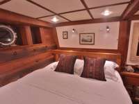 Cozy wooden cabin with double bed porthole, and traditional decor aboard the Ombak Putik sailing yacht in Indonesia. 