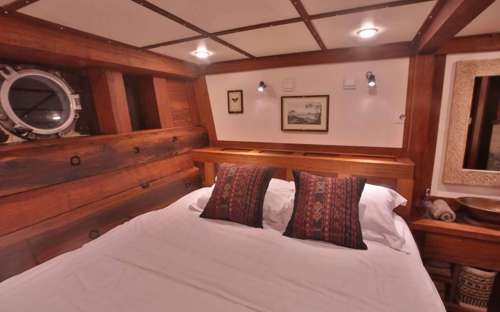 Cozy wooden cabin with double bed porthole, and traditional decor aboard the Ombak Putik sailing yacht in Indonesia. 
