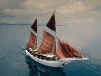 The Ombak Putik, a traditional Indonesian sailing ship, glides across calm blue waters under soft skies near the Komodo Islands. 