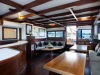  Spacious interior lounge on a traditional Indonesian cruise ship, featuring wood paneling, cozy sofas, and natural light. 