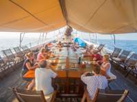 Guests enjoying open-air dining on the deck of an Indonesian cruise ship under a shaded awning with ocean views all around. 