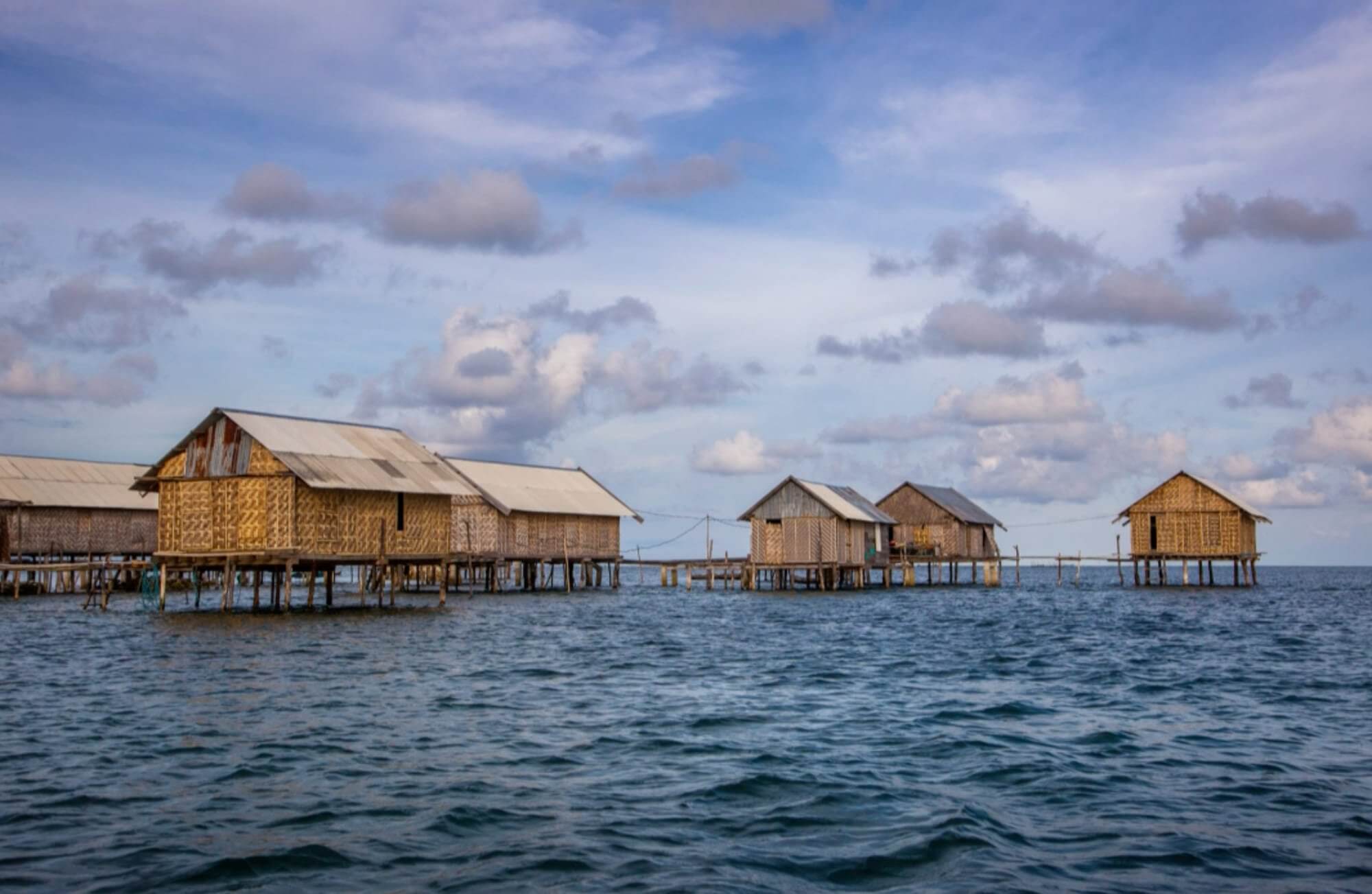 Traditional stilt houses of the Bajo people floating above the sea in Sulawesi, Indonesia, under a scenic cloudy sky. 