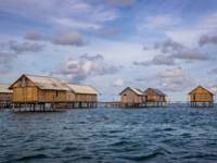 Traditional stilt houses of the Bajo people floating above the sea in Sulawesi, Indonesia, under a scenic cloudy sky. 