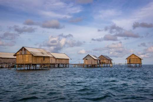 Traditional stilt houses of the Bajo people floating above the sea in Sulawesi, Indonesia, under a scenic cloudy sky. 