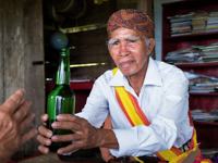 A Balinese elder in ceremonial dress presents a traditional drink. 