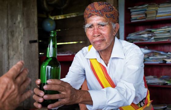 A Balinese elder in ceremonial dress presents a traditional drink. 
