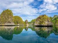 Crystal-clear waters reflect limestone islets and blue skies in Misool, Indonesia, creating a perfect mirror-like tropical seascape. 