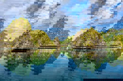 Crystal-clear waters reflect limestone islets and blue skies in Misool, Indonesia, creating a perfect mirror-like tropical seascape. 